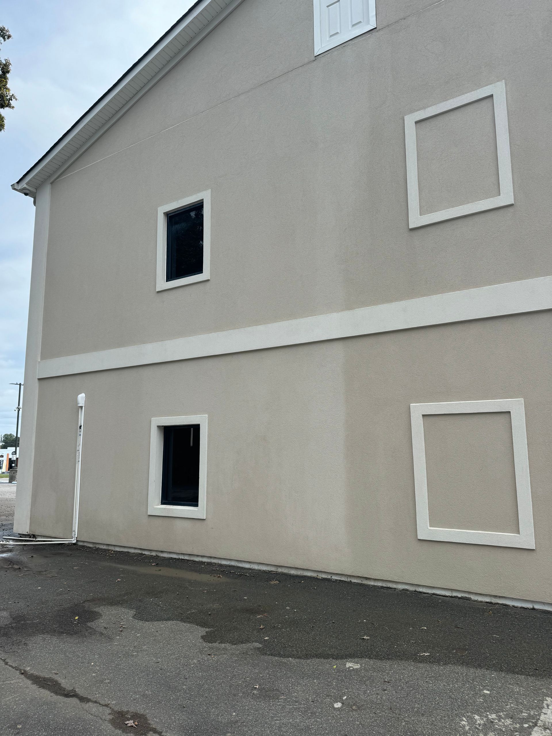 Side view of a gray stucco house with four square windows and a paved driveway.