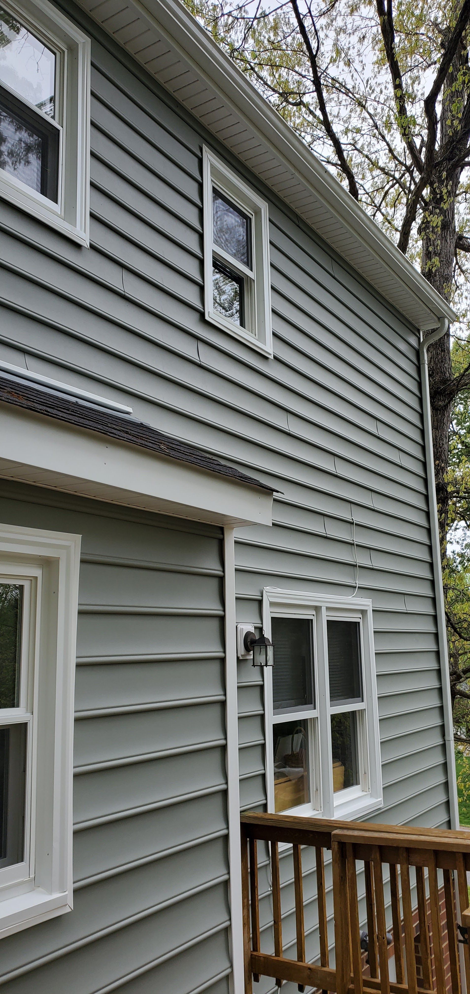 Gray vinyl-sided house exterior with white-trimmed windows and a small wooden deck railing.