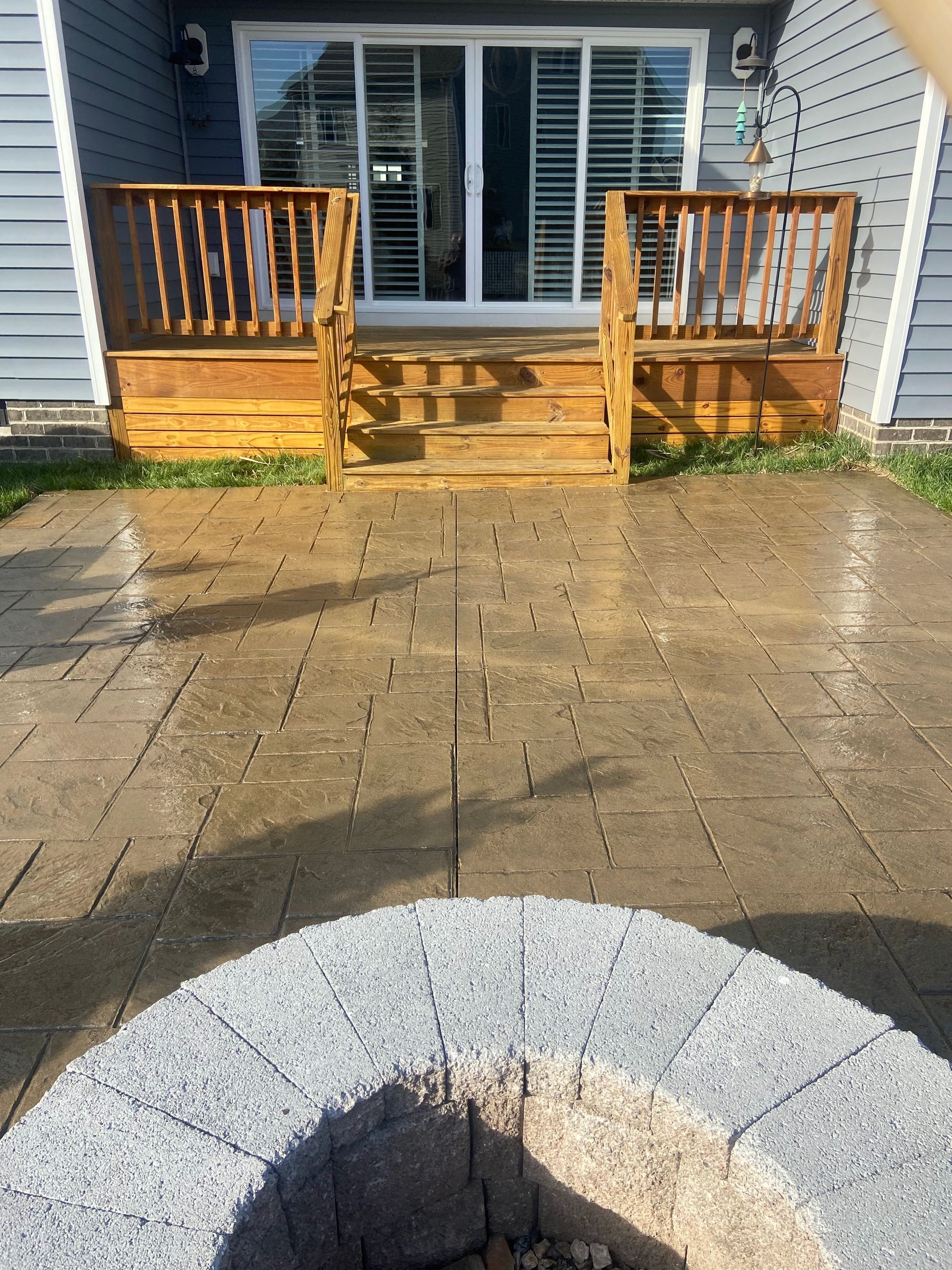 Wooden front porch with steps and railings leading to a glass sliding door, with a paved patio in front