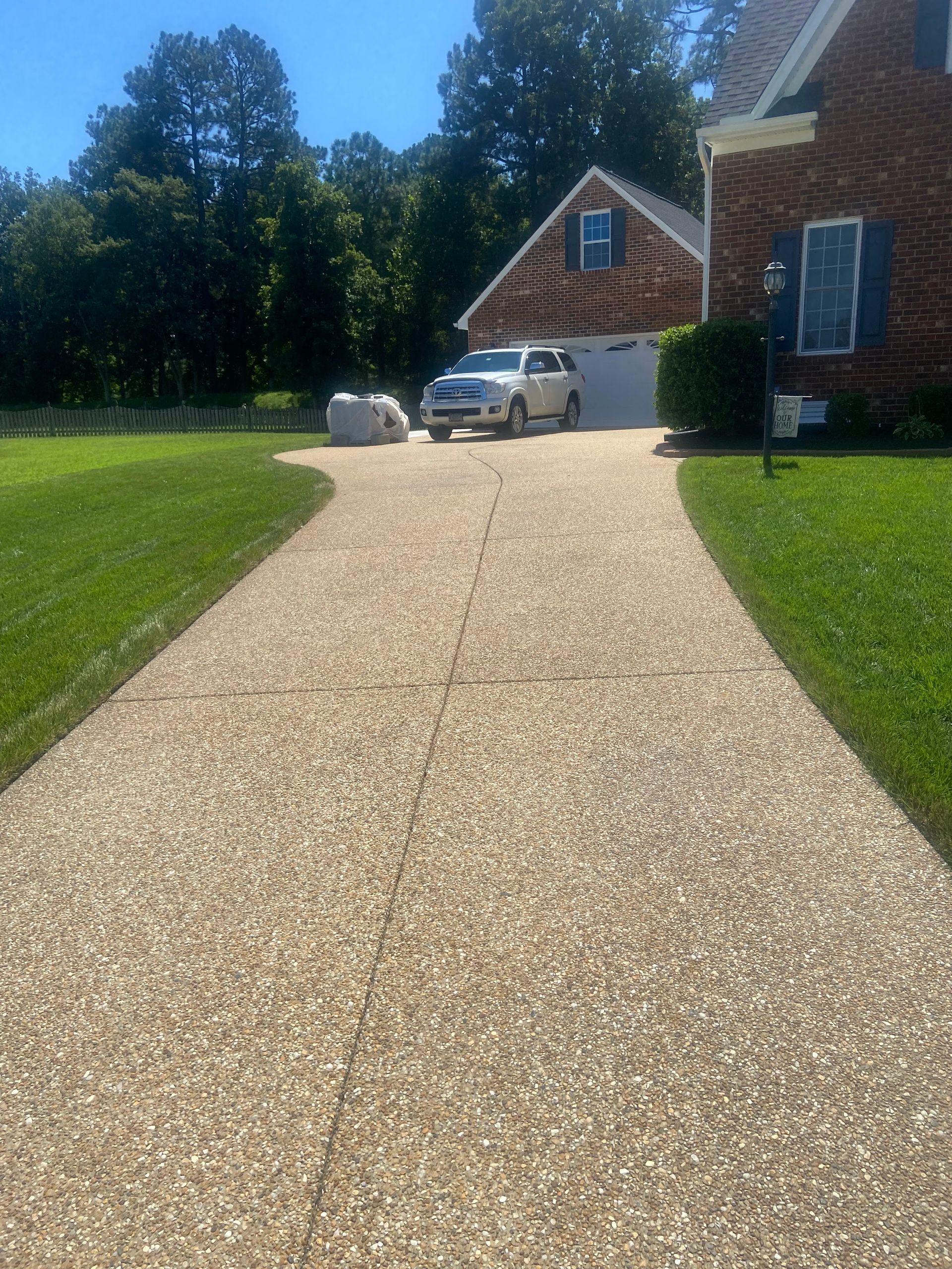 Gravel driveway leading to a brick house, with a parked car and green lawn on a sunny day