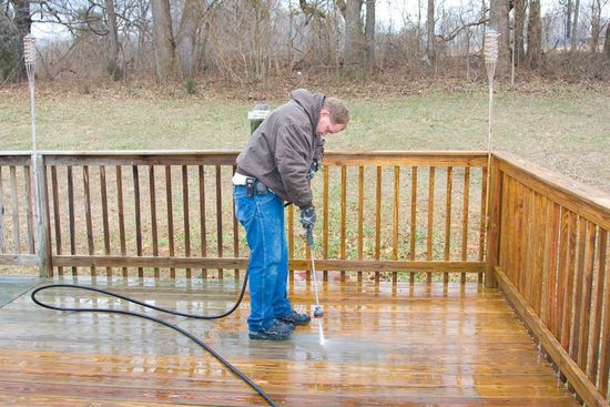 Person pressure-washing a wet wooden deck on a rainy day.