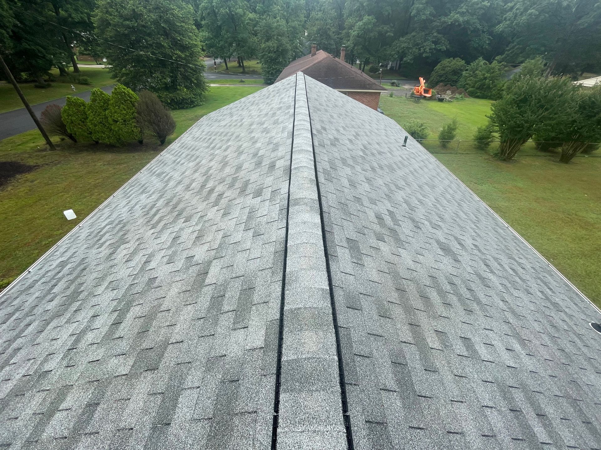 View from a rooftop with gray shingles over a green yard and trees