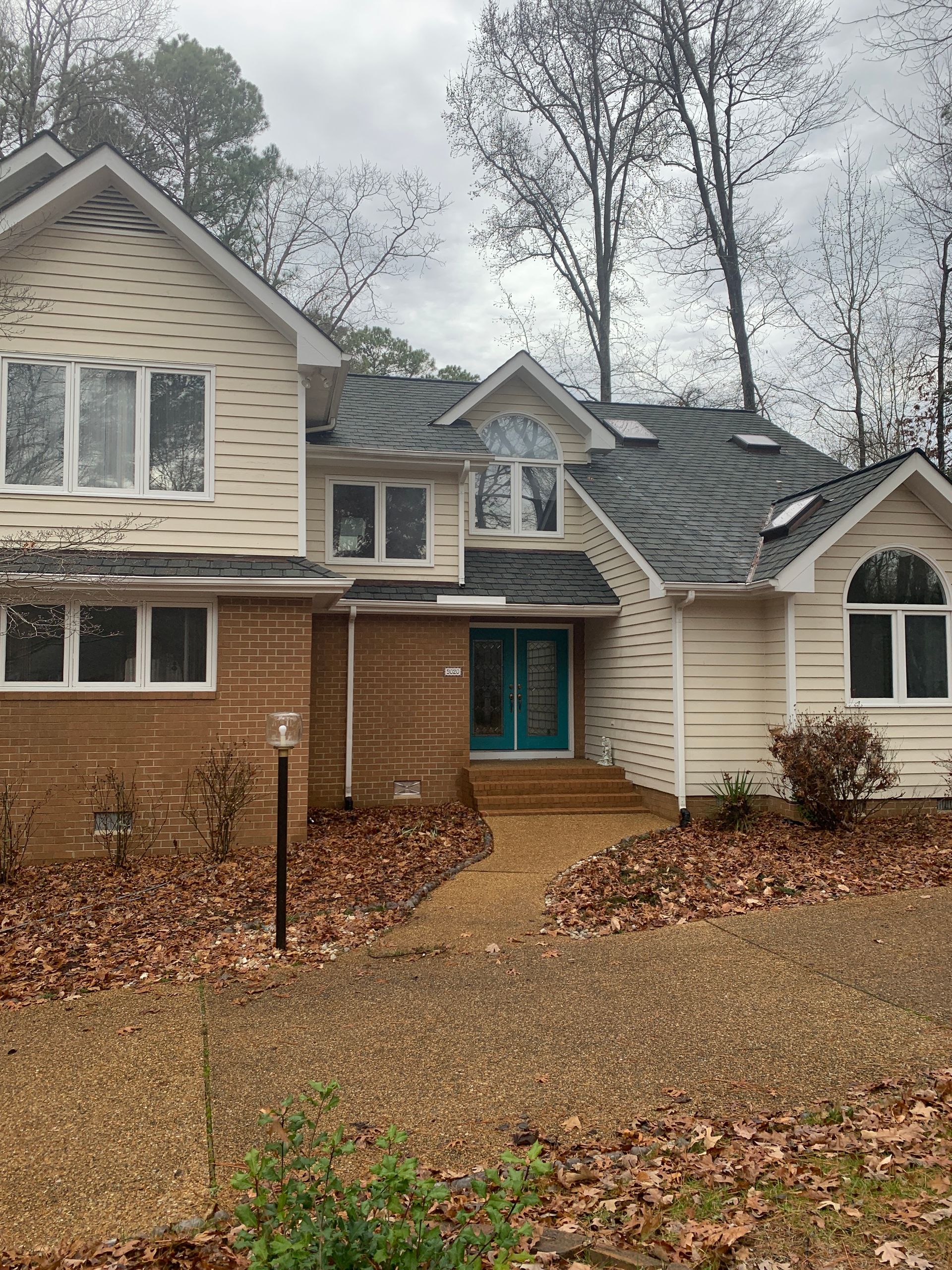 Suburban brick-and-siding house with teal front door and leaf-covered yard on a cloudy day