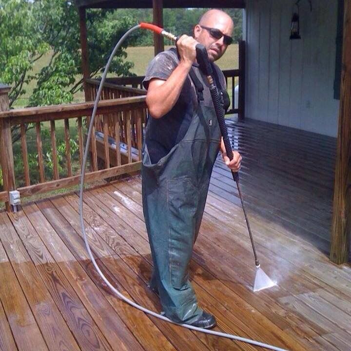 Man using a pressure washer to clean a wet wooden deck on a porch