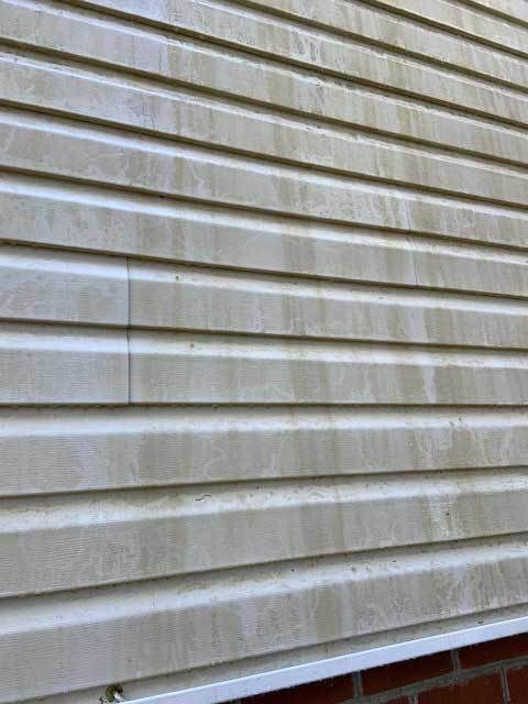 Close-up of beige vinyl house siding with horizontal lines and water stains