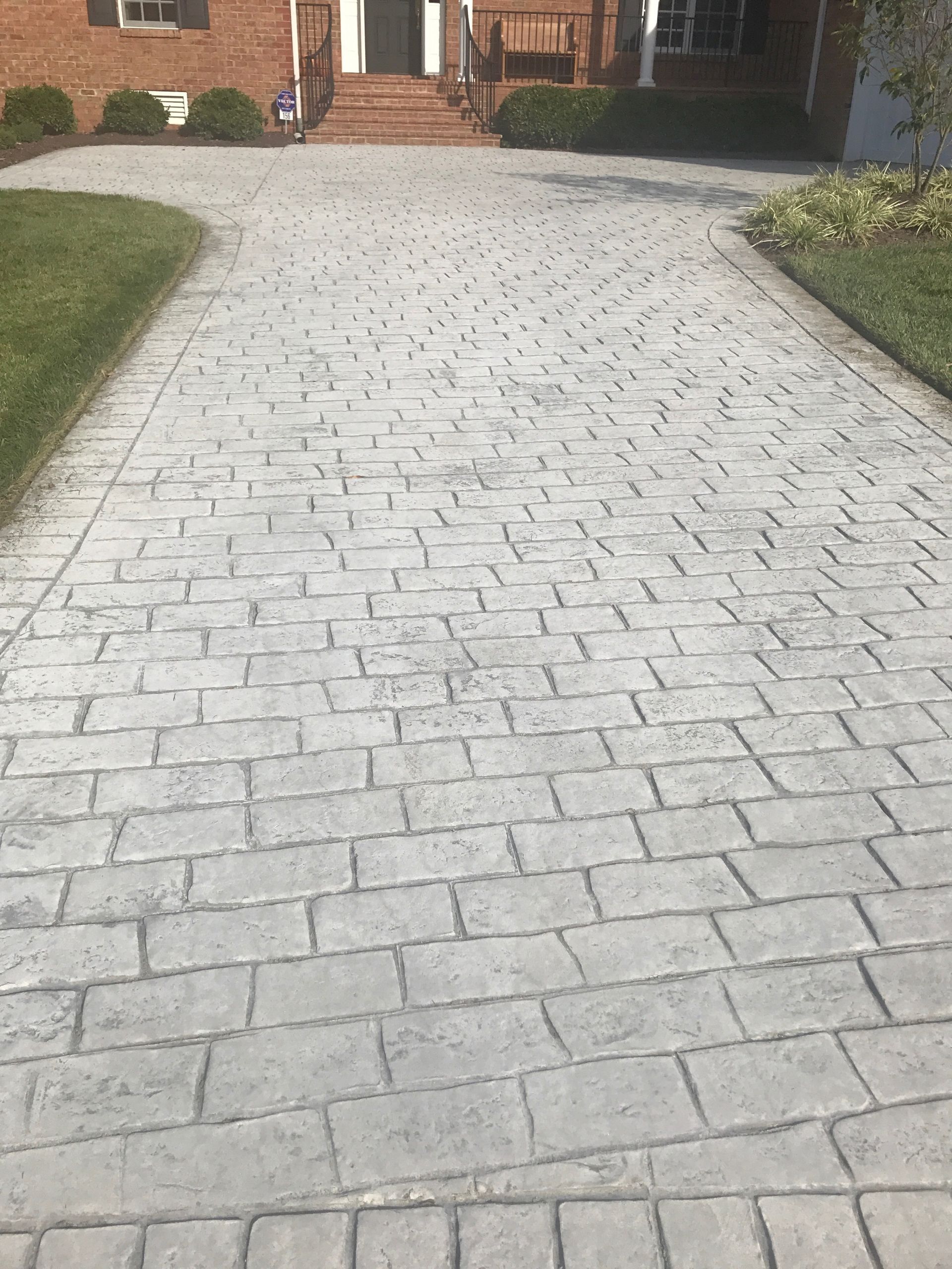 Stone-paved driveway leading to a house entrance, bordered by grass and shrubs.