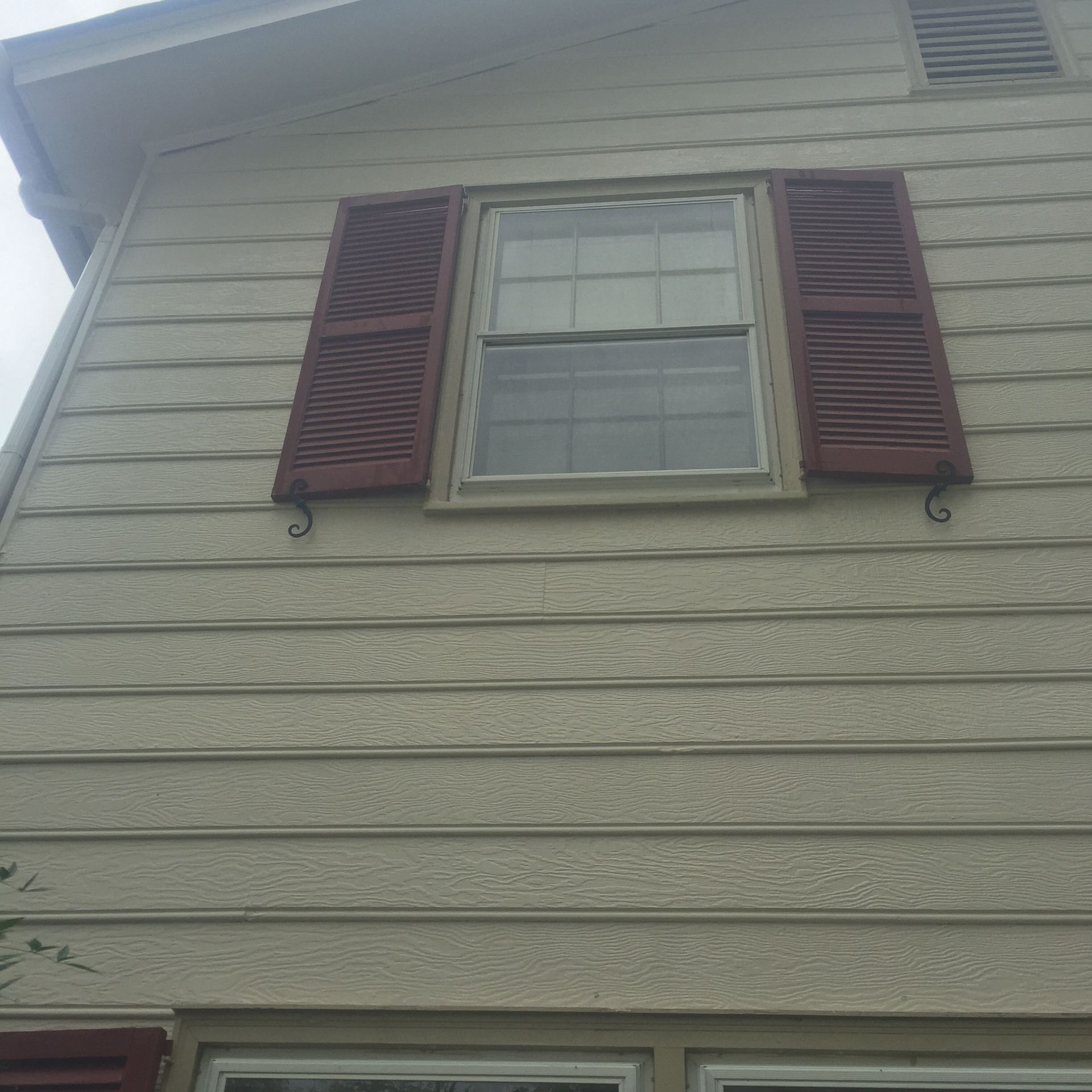 Exterior of a beige house with maroon shutters around a second-story window