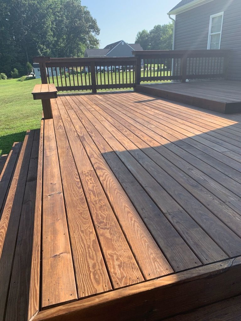 Sunlit wooden deck with gray and natural wood planks beside a house and railing