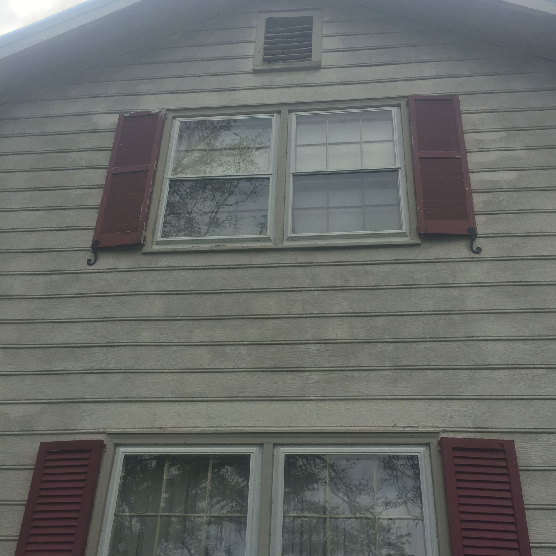 Gray house exterior with white-framed windows and red shutters, seen from below