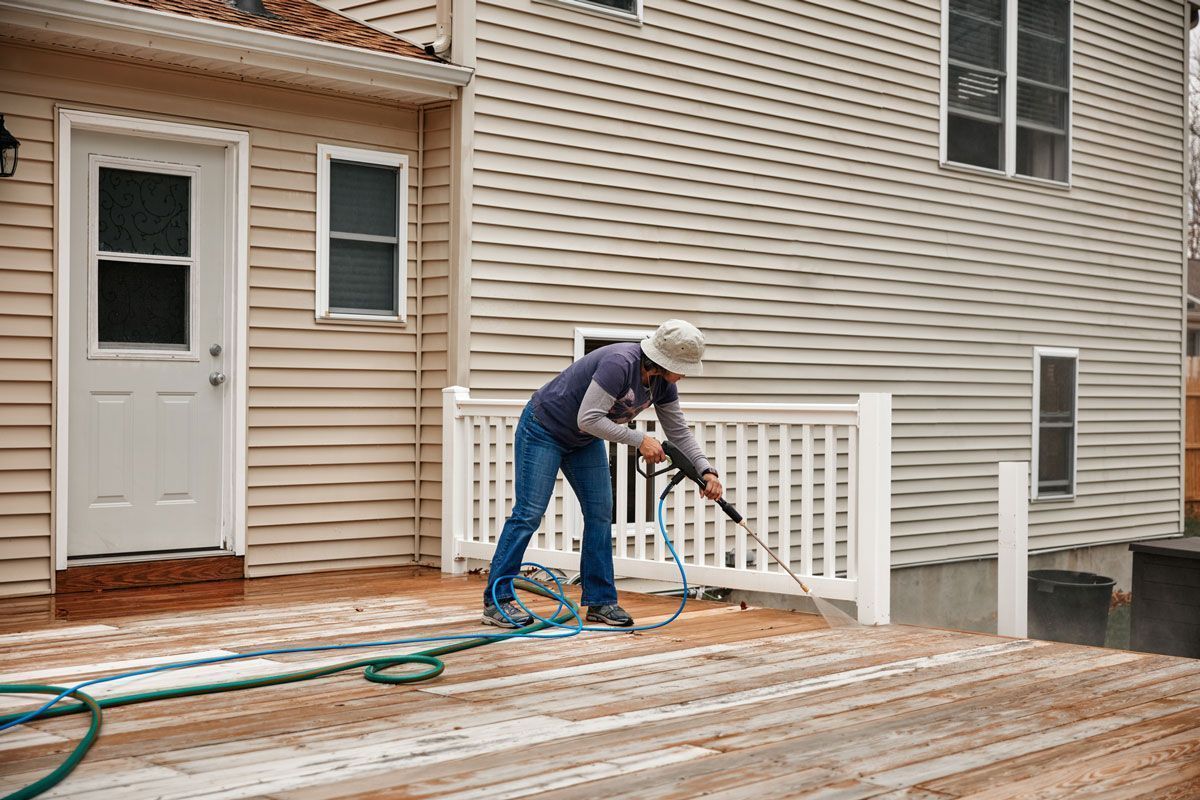 Person sanding a wooden deck beside a house with a power sander