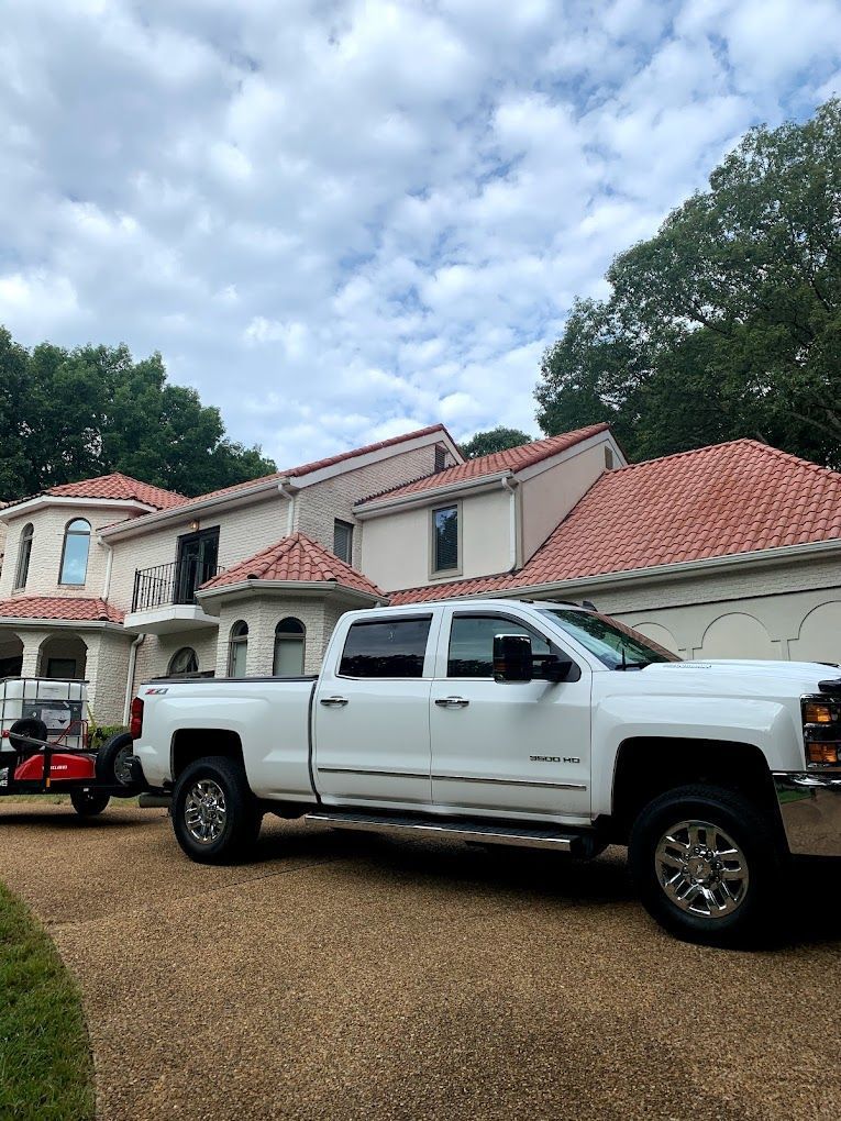 White pickup truck parked in front of a large two-story house with a red tile roof under a cloudy sky