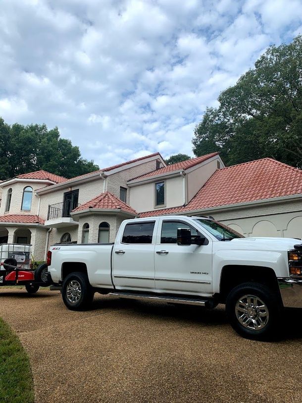 White pickup truck parked in front of a large two-story house with a red tile roof under a cloudy sky