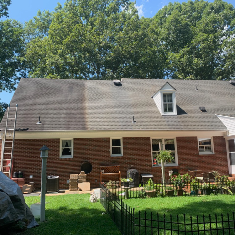 Brick house with gray roof, white dormer windows, and a fenced backyard under blue sky