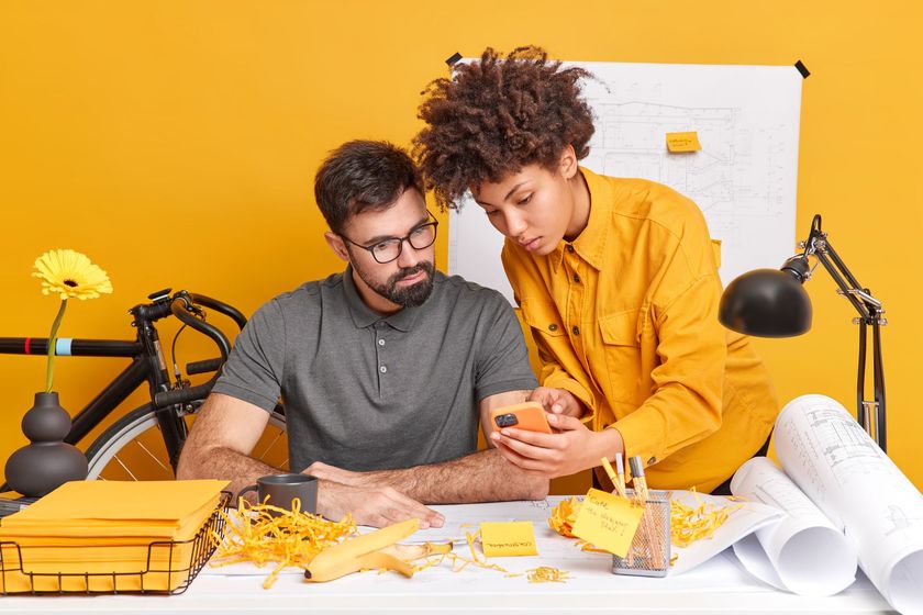 A man and a woman are sitting at a table looking at a cell phone.