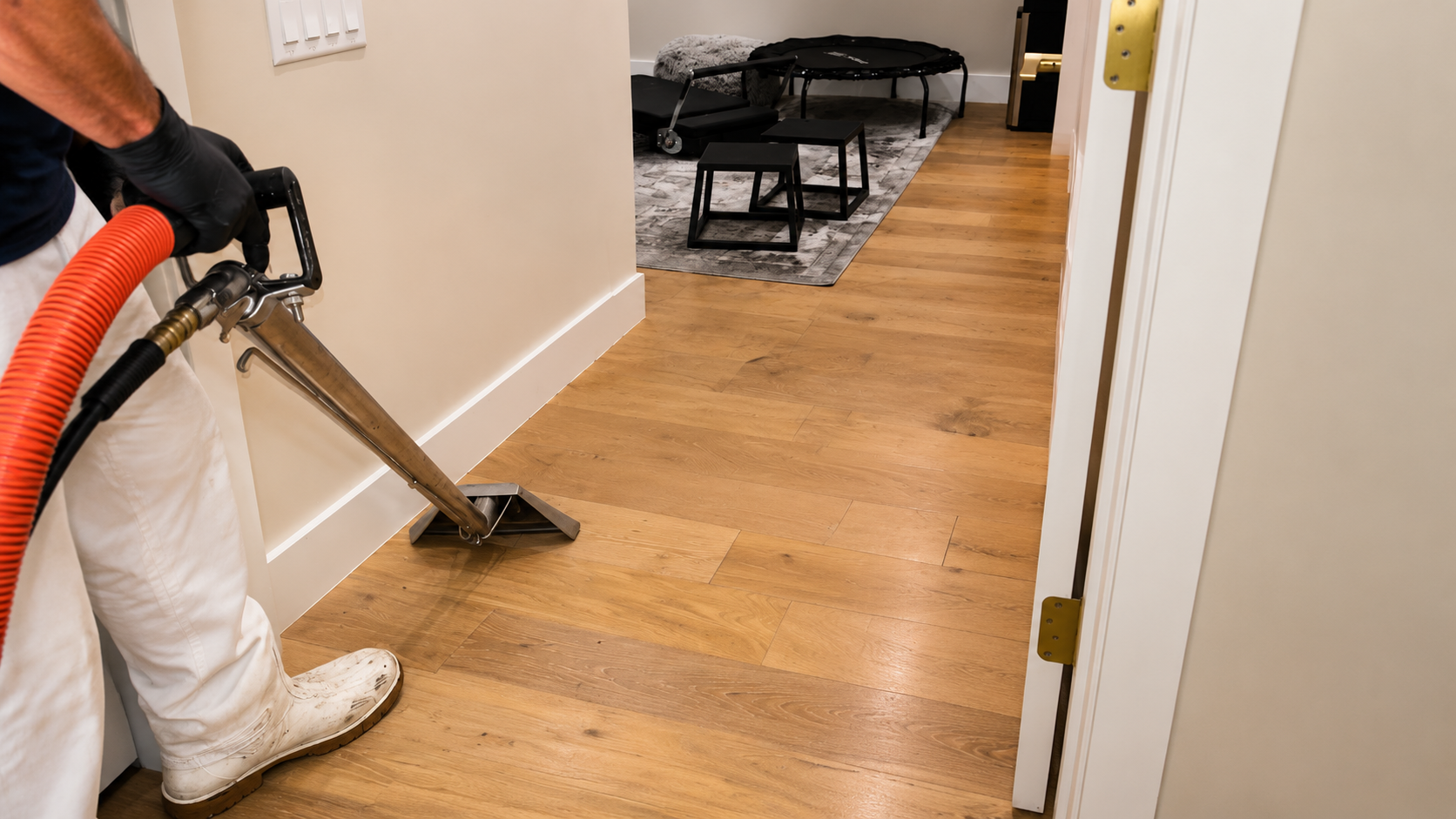 Person using a vacuum wand to clean a hardwood hallway, with a black piano in the background.