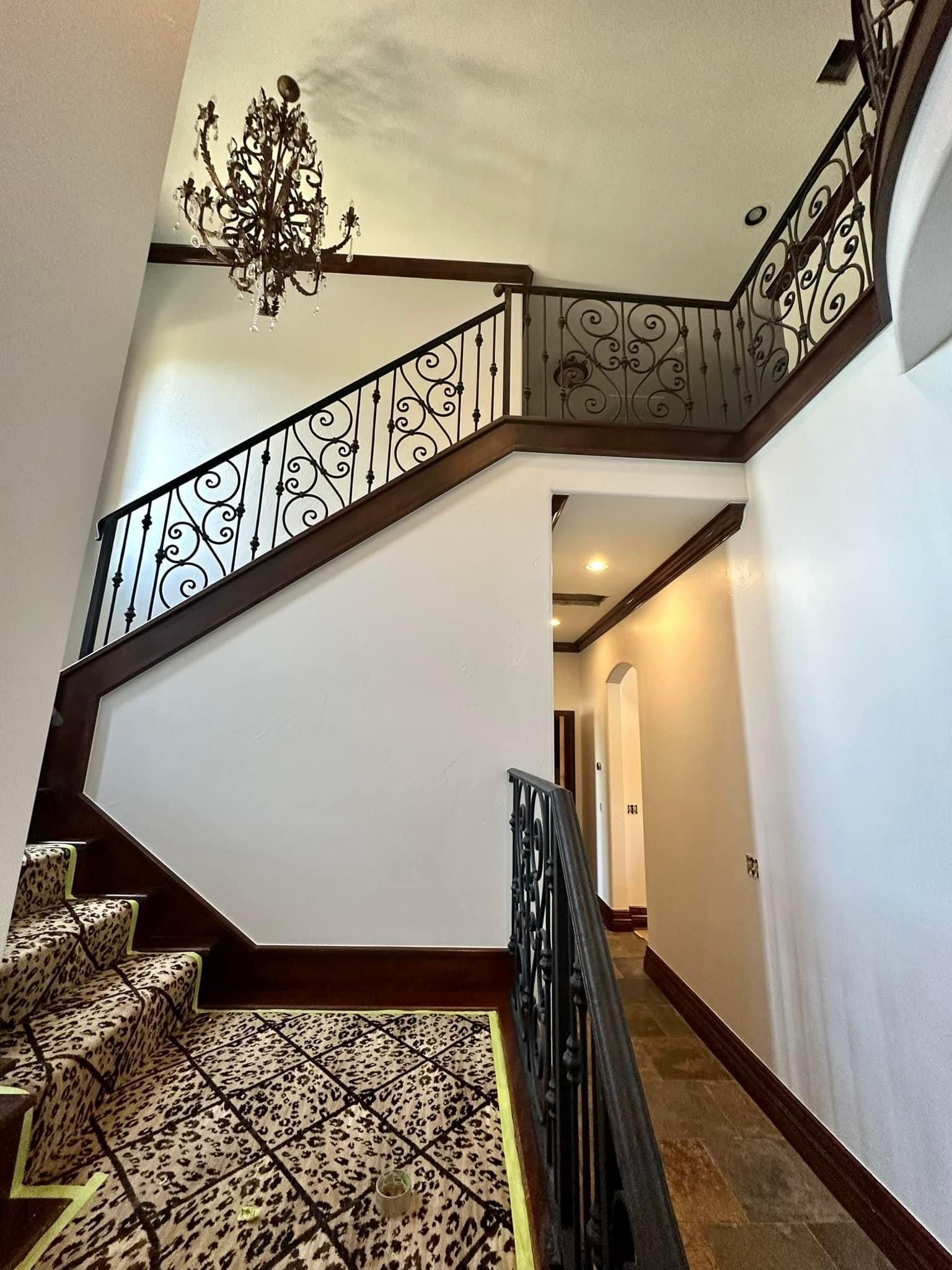 A staircase with a wrought iron railing and a chandelier hanging from the ceiling.