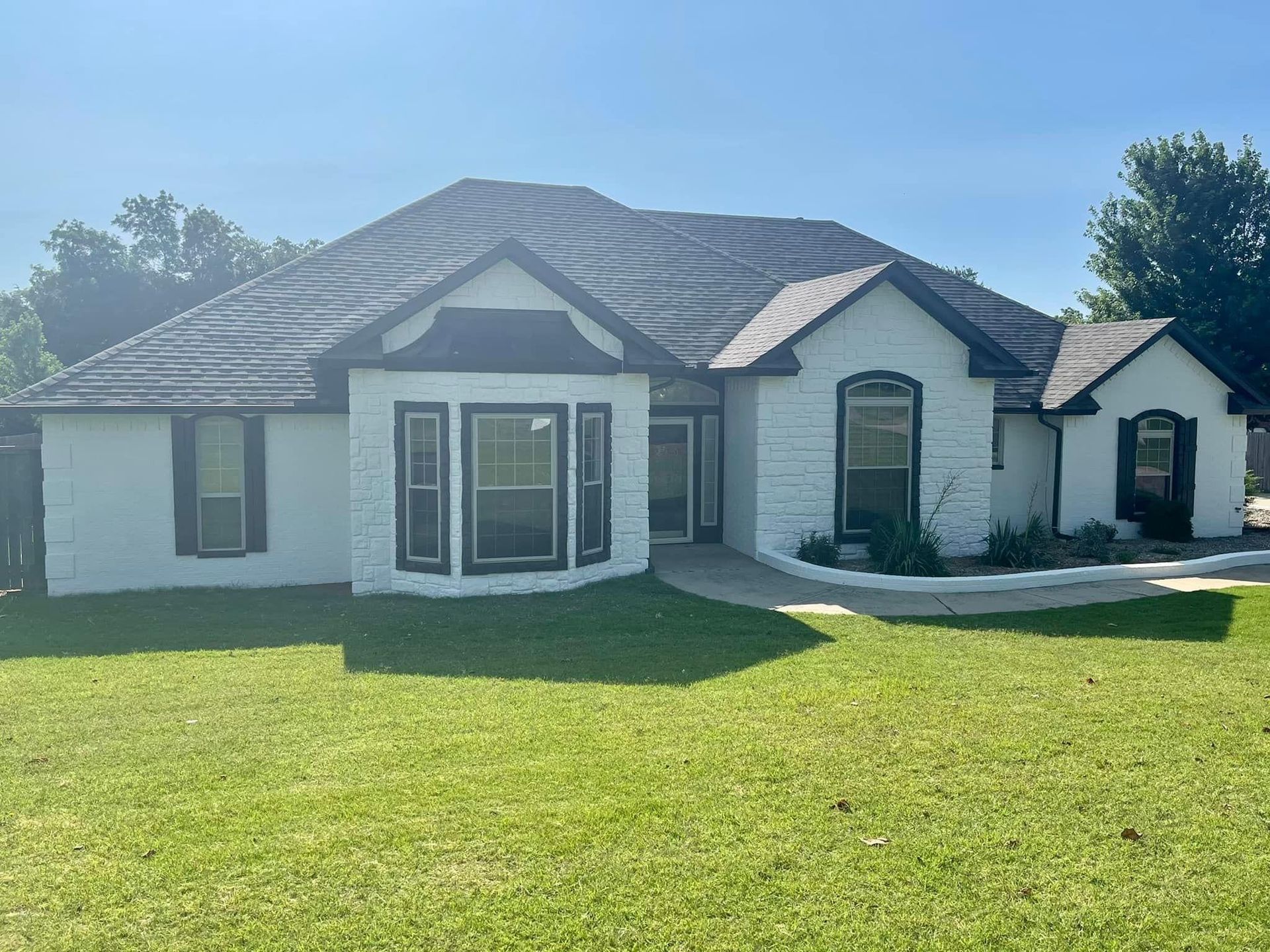 A white house with black shutters and a large lawn in front of it.