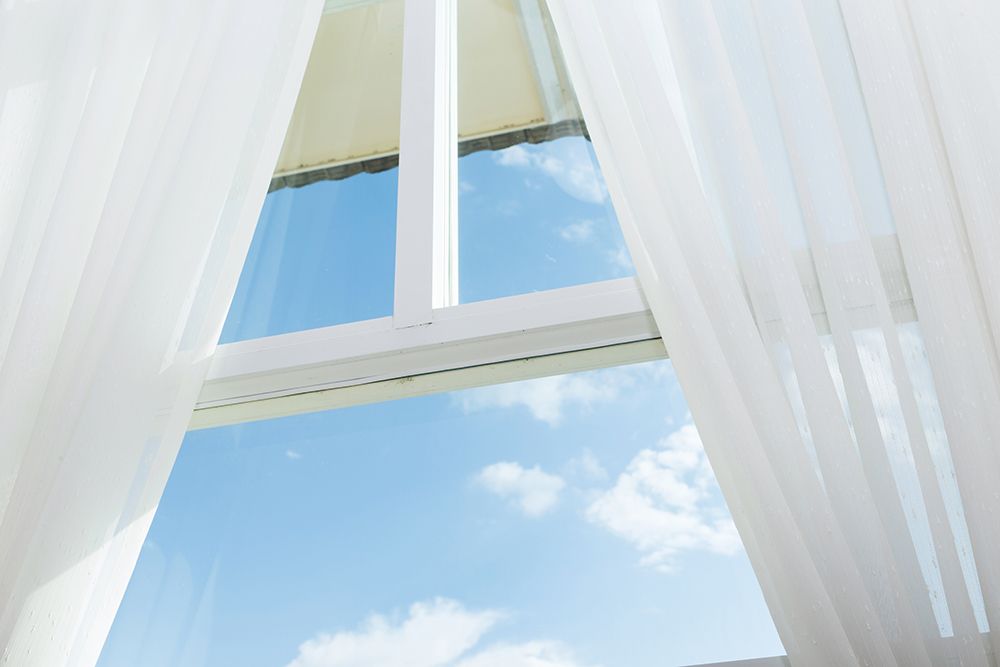 A window with white curtains open and a blue sky behind it.