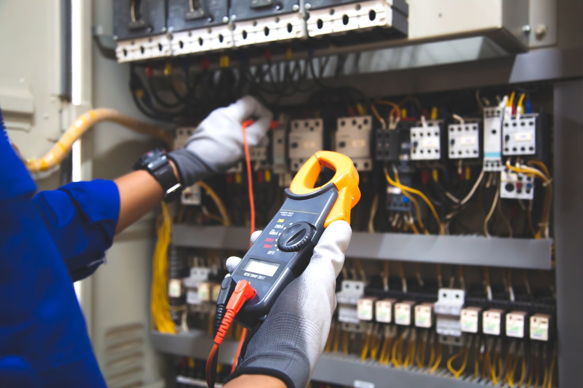 An electrician is using a clamp meter to test a circuit board.