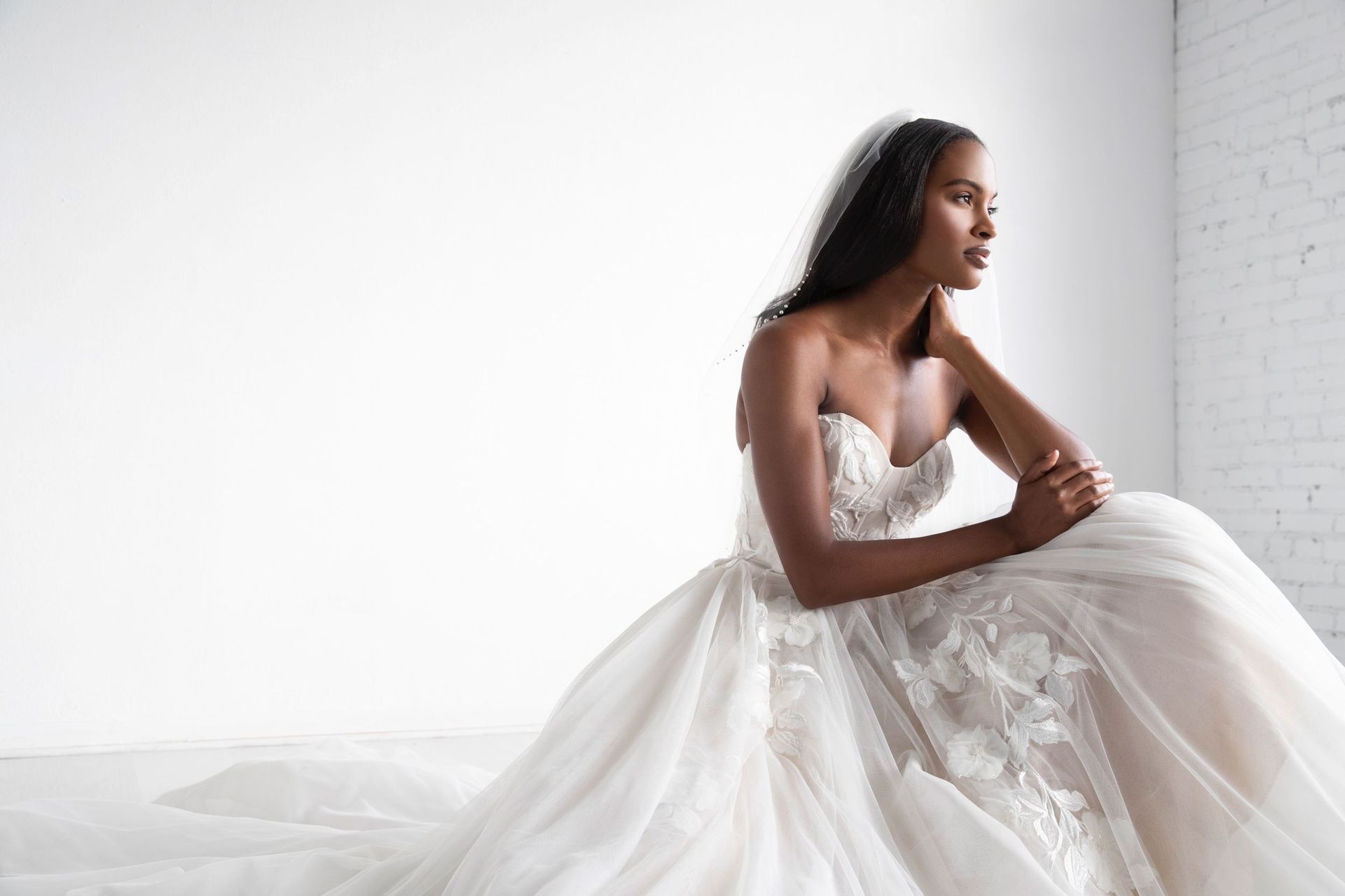 A woman in a wedding dress is sitting on a bed.