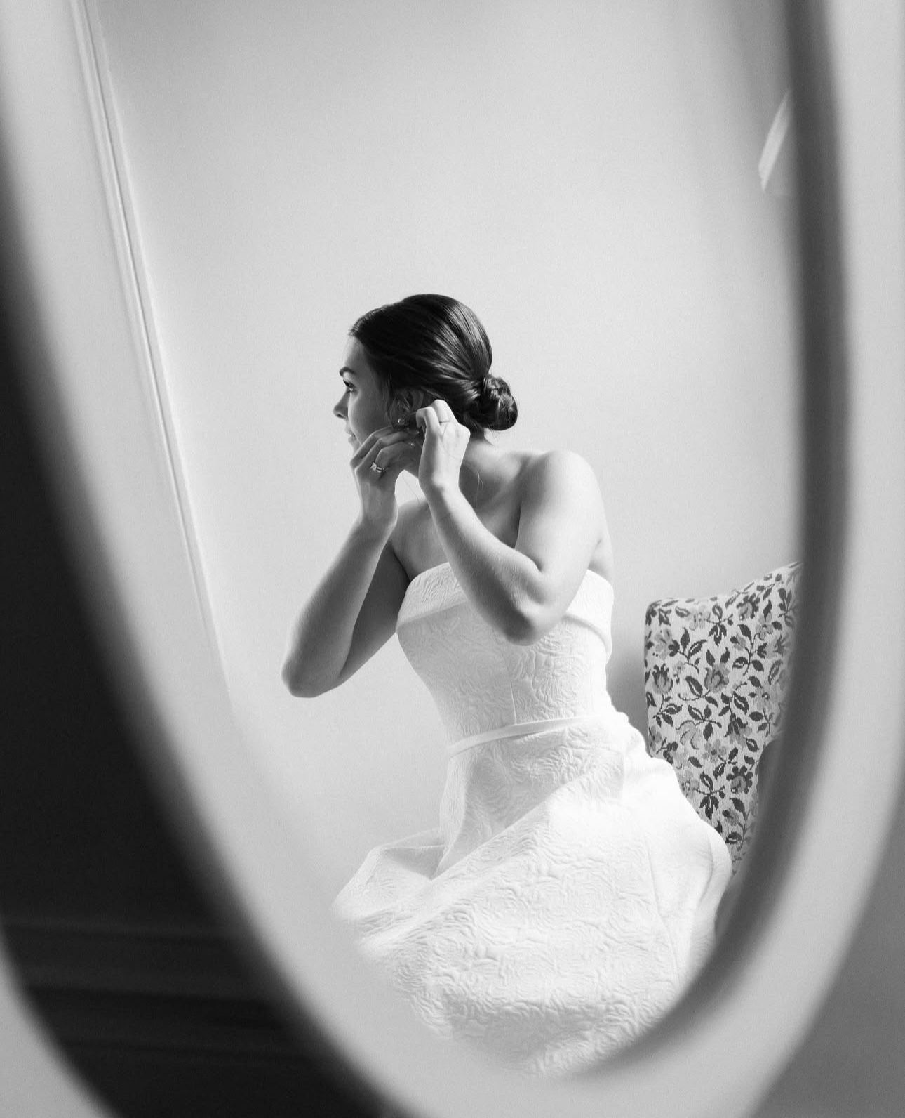 A bride is putting on her earrings in front of a mirror.