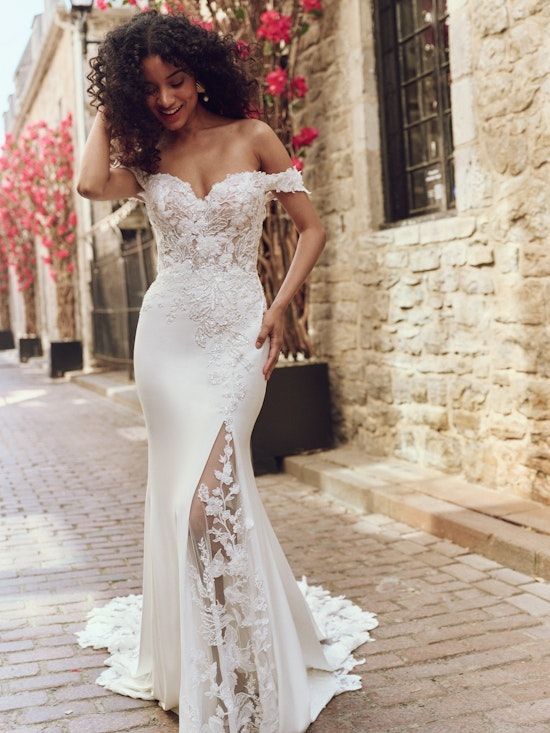 A woman in a white wedding dress is standing on a brick sidewalk.