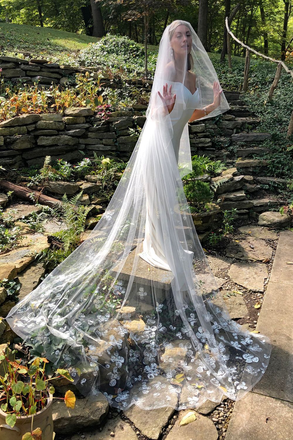 A woman in a wedding dress and veil is standing on a rock.
