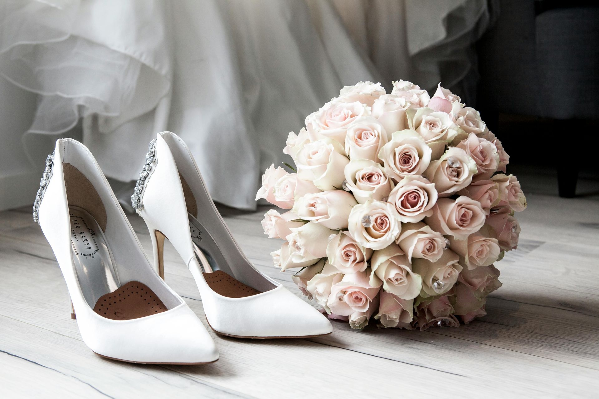 A bouquet of roses next to a pair of wedding shoes.