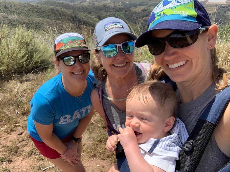 Three women are posing for a picture with a baby in a carrier.