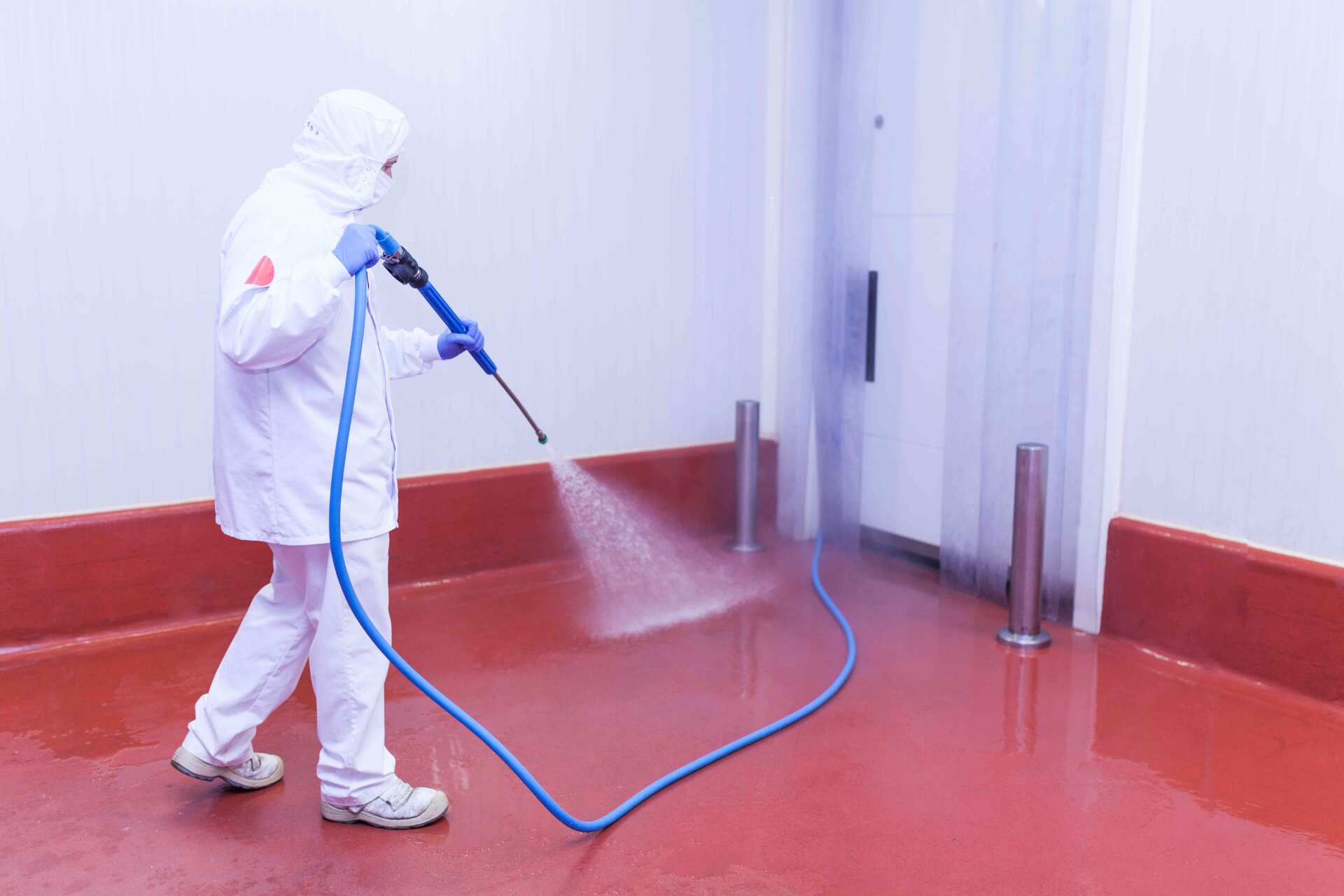 A Man in a Suit is Spraying Water on a Floor — O & D House Wash & Cleaning Services in Glenvale, QLD