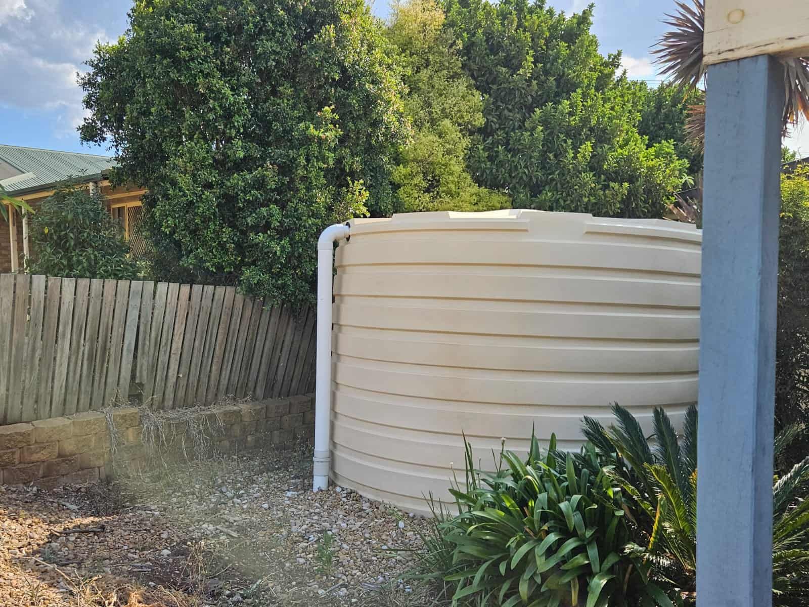 A large white water tank is sitting next to a wooden fence. — O & D House Wash & Cleaning Services in Glenvale, QLD