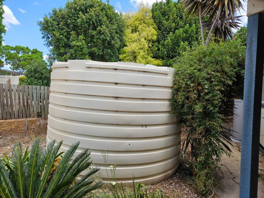 A Large White Water Tank is Sitting in the Middle of a Garden — O & D House Wash & Cleaning Services in Glenvale, QLD