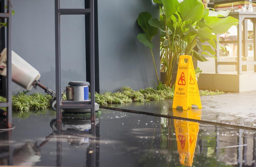 A Wet Floor With a Yellow Caution Sign on It — O & D House Wash & Cleaning Services in Glenvale, QLD