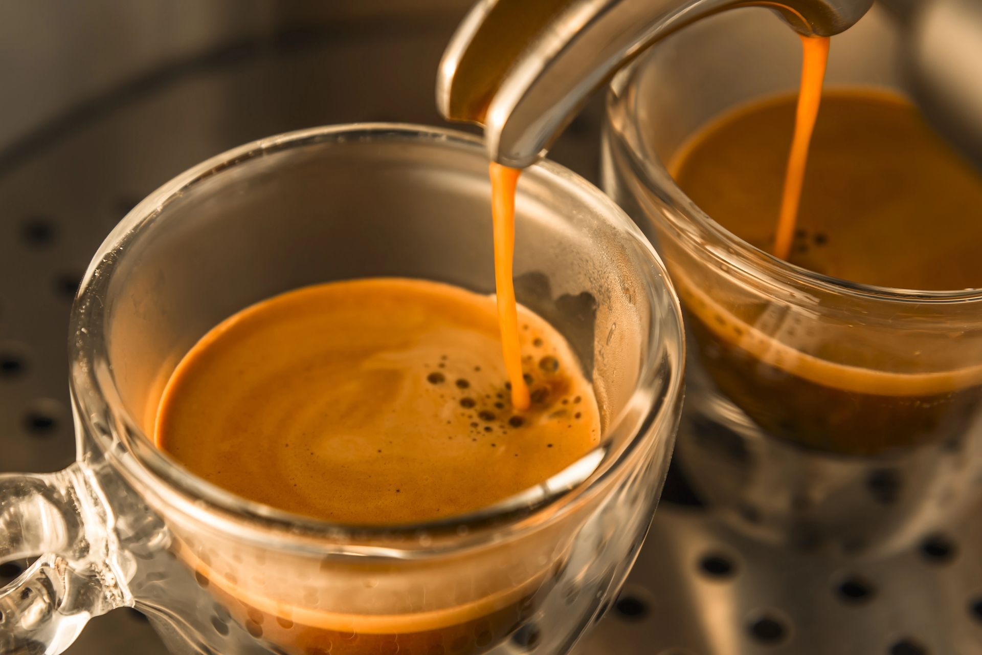 Una macchina per caffè espresso a doppio beccuccio versa caffè fresco, di colore marrone dorato, in due tazze di vetro trasparente poste su un vassoio metallico.