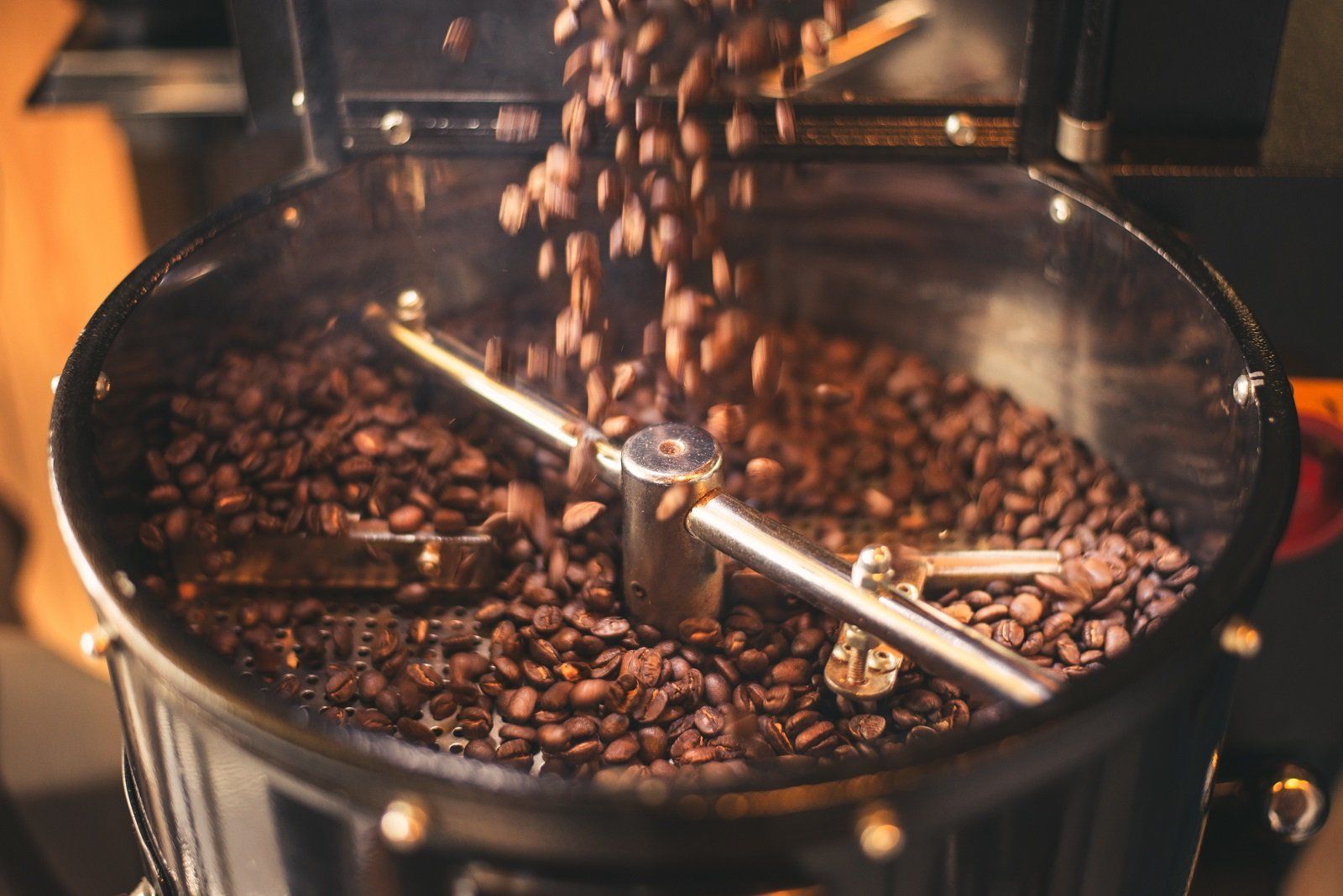 Chicchi di caffè appena tostati vengono versati in un vassoio di raffreddamento metallico dotato di bracci rotanti.