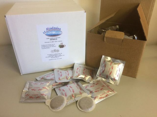 Una scatola bianca con un'etichetta stampata si trova accanto a una scatola di cartone aperta contenente diverse capsule di caffè singole.