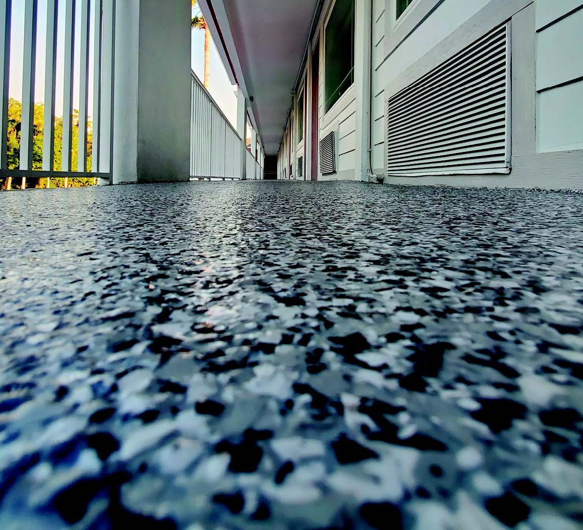 Low-angle view of a building walkway with textured floor, railings, and vents along the side