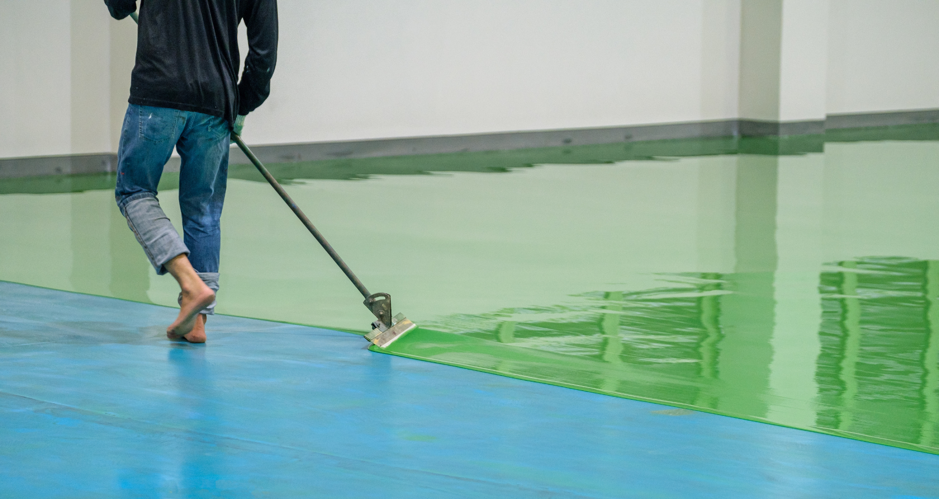 Person rolls green floor coating across a blue-and-green floor with a roller.