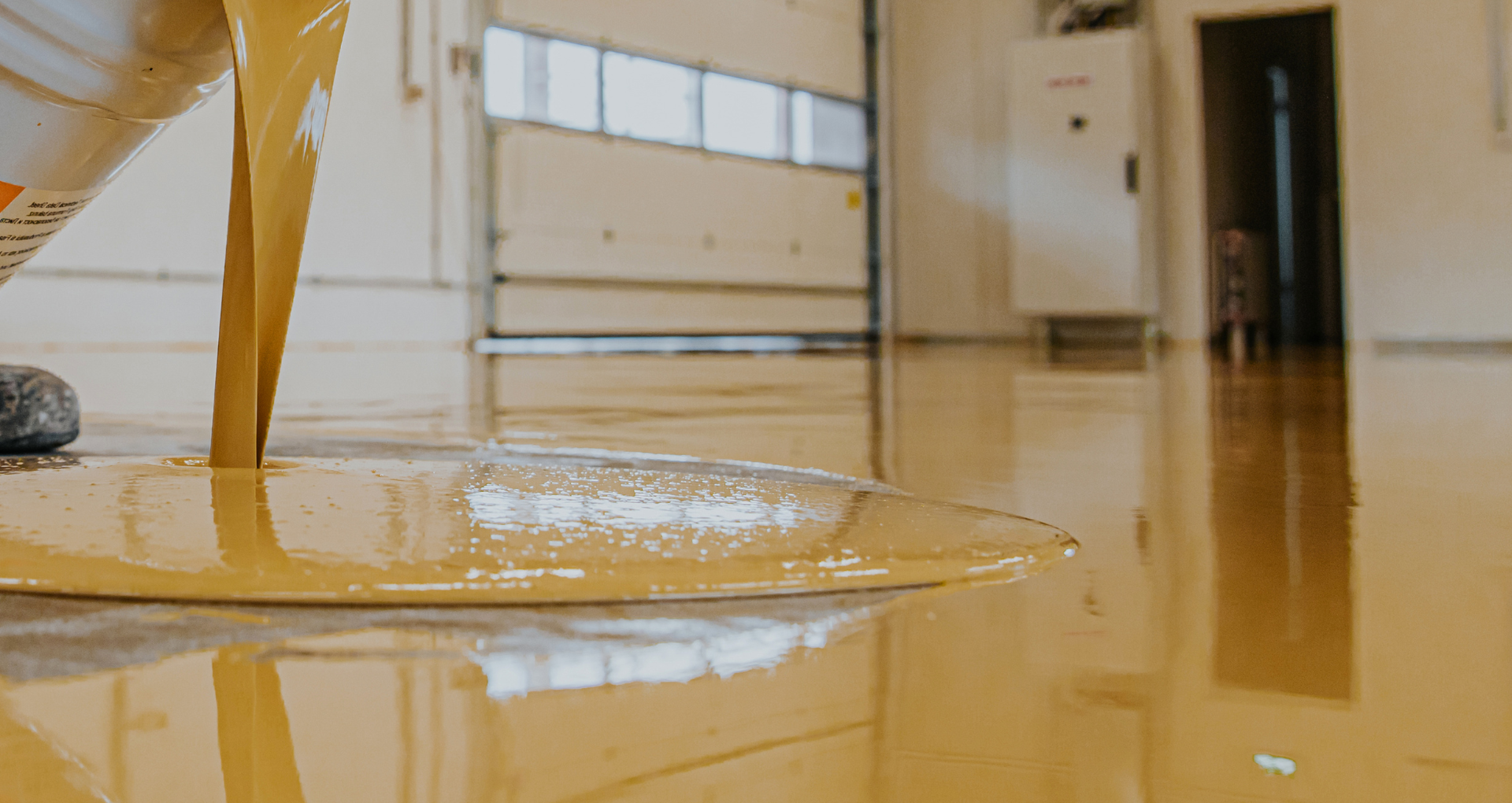 Liquid spilled across a polished floor in a bright room, reflecting nearby windows and furniture.
