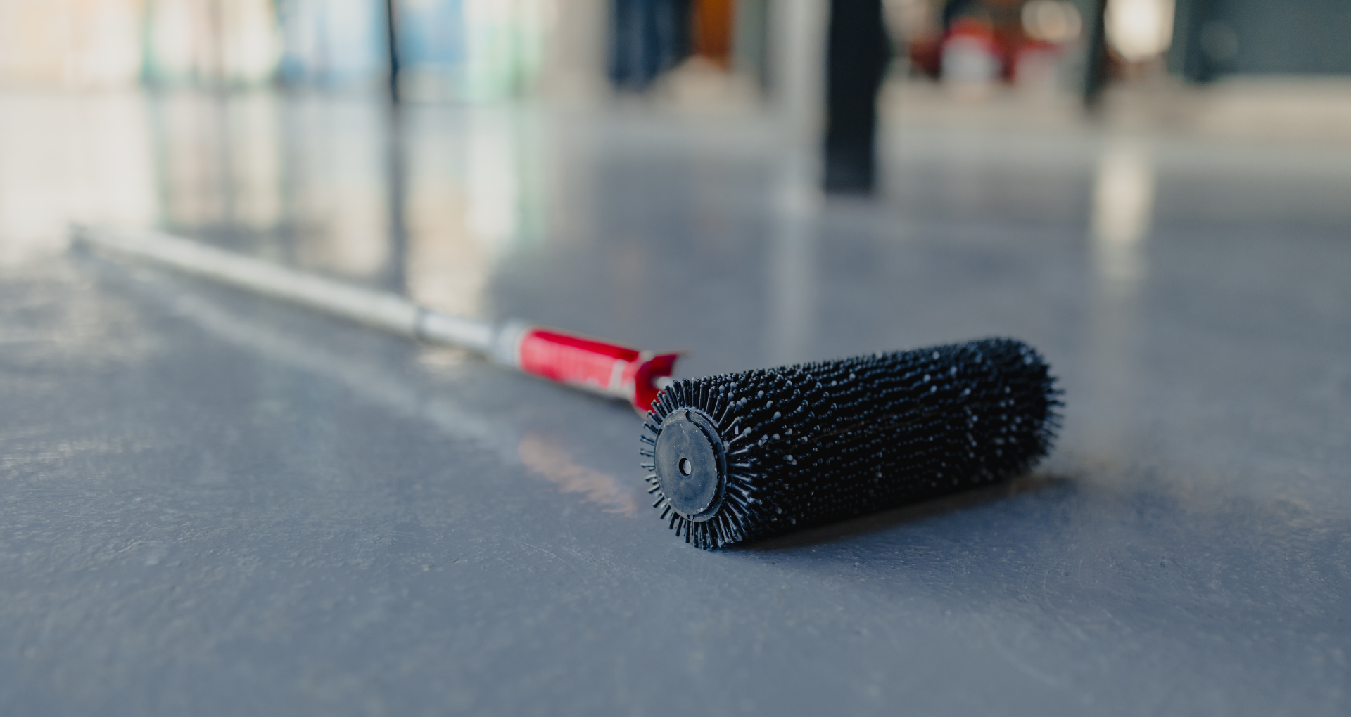 Black hairbrush with a red handle lying on a gray floor in a blurred indoor hallway