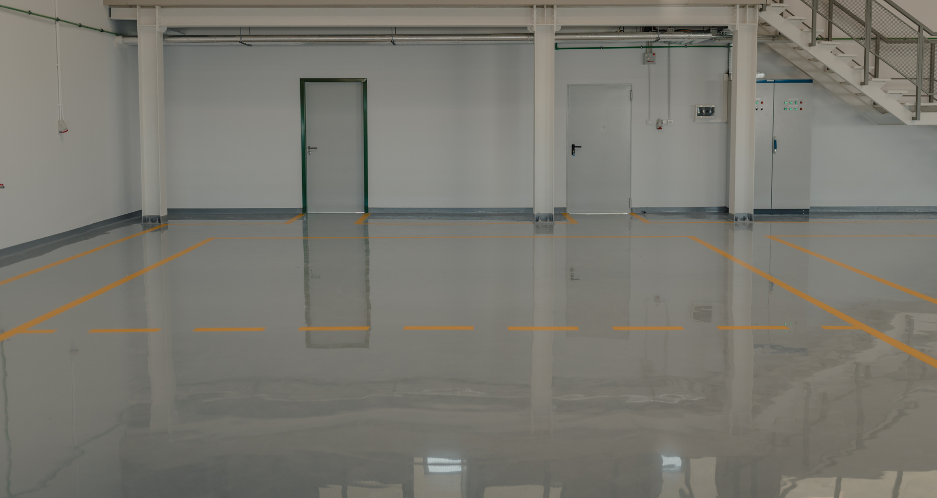 Empty industrial room with glossy gray floor, white walls, orange floor lines, and a closed door.