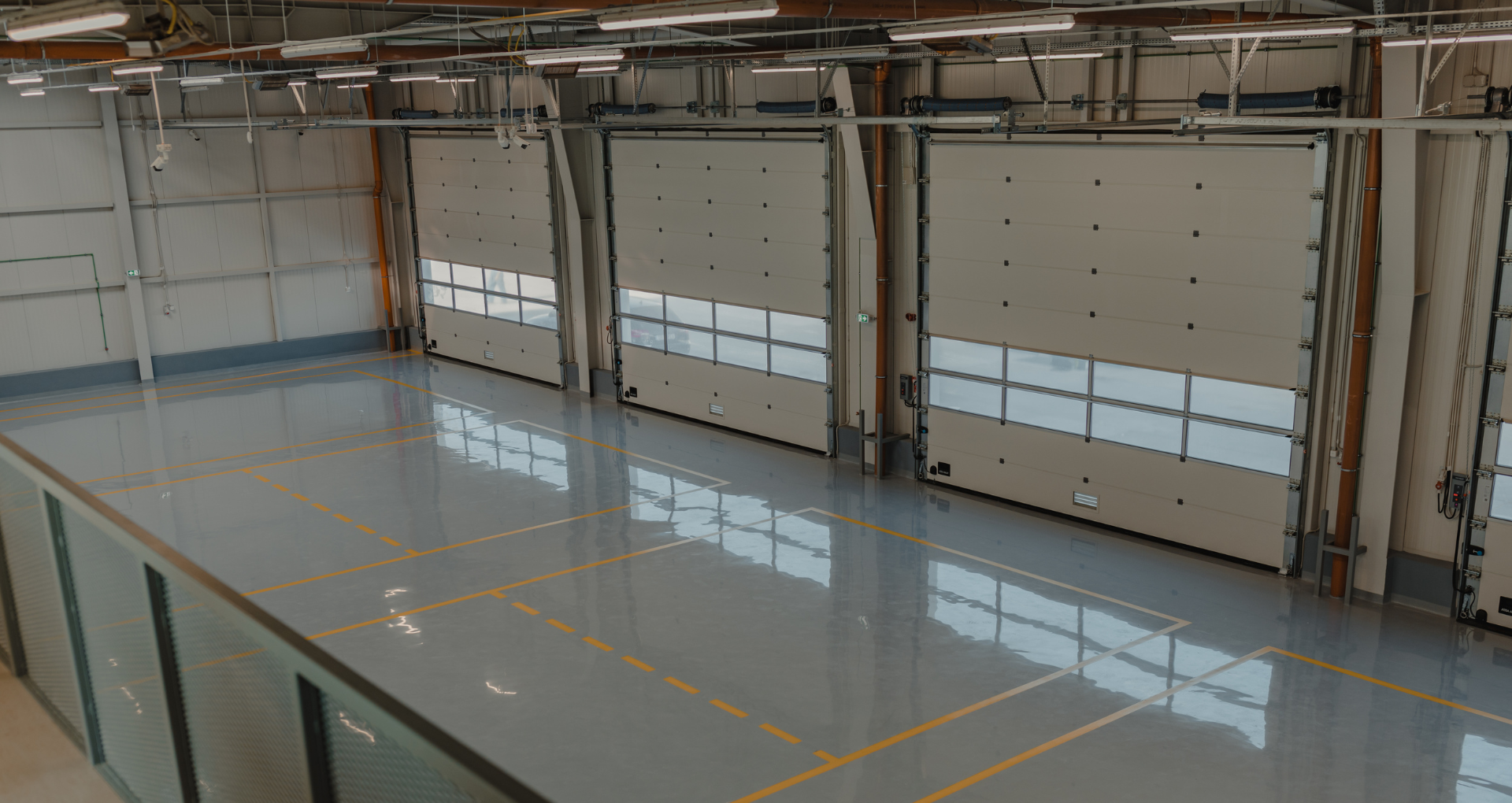 Empty warehouse with polished floor and large industrial roll-up doors along the wall