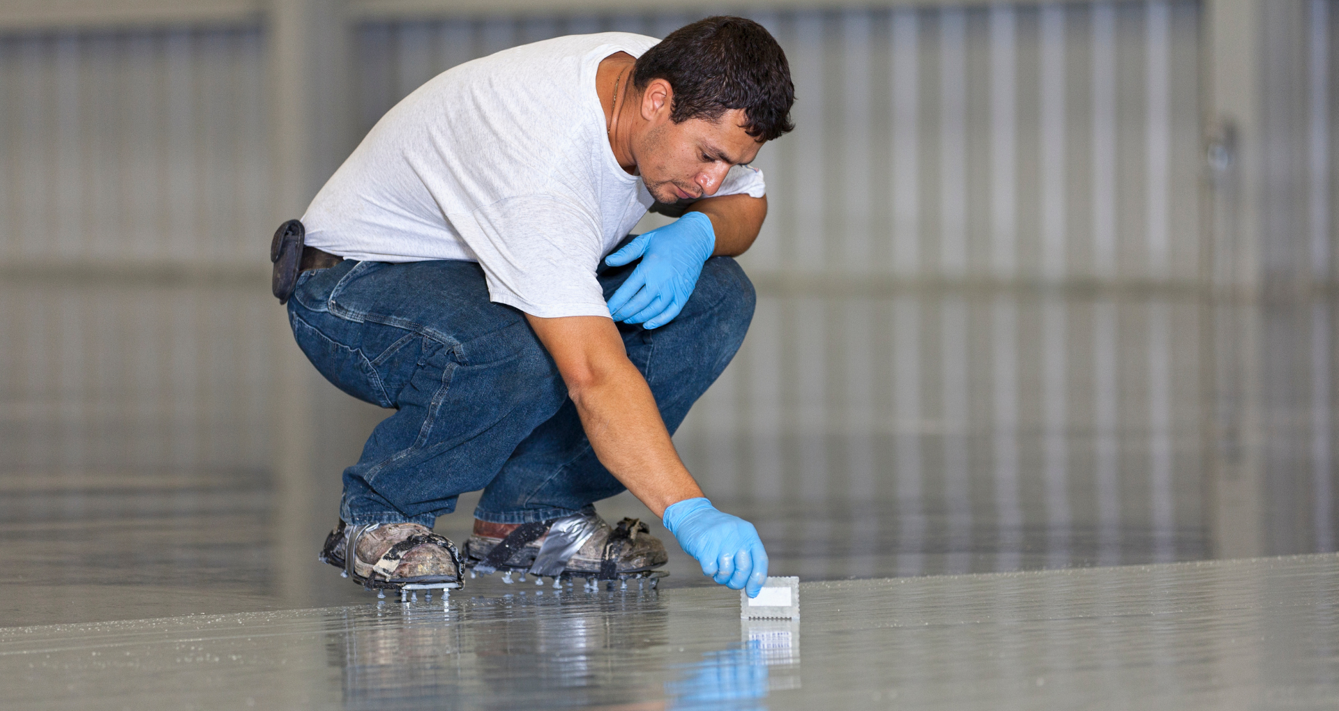 Worker crouching on a polished floor, inspecting a small white block with blue gloves.