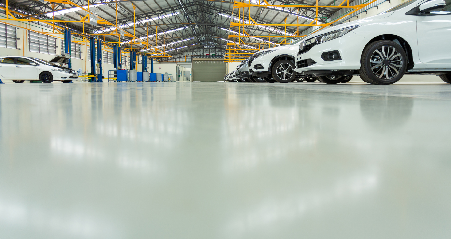 Bright car showroom with white cars parked under a high metal roof, reflected on polished floor