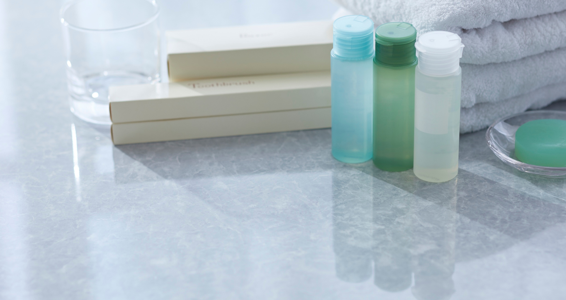 Bathroom shelf with folded white towels, toiletry bottles, and a green soap dish on a reflective surface