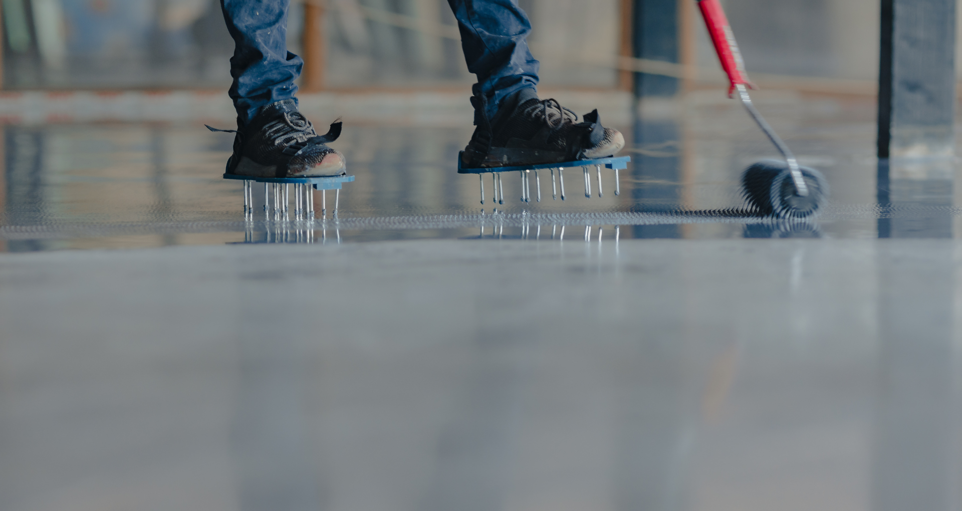 Person ice skating with a red hockey stick on an indoor rink, close-up of skates on the ice