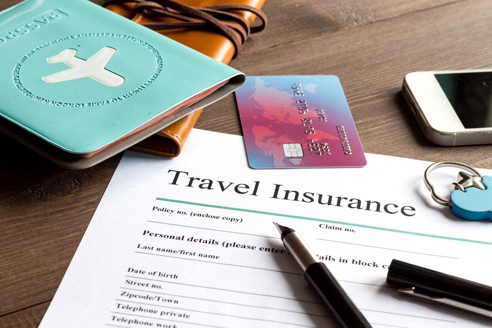 A travel insurance form with a credit card , passport , cell phone and pen on a wooden table