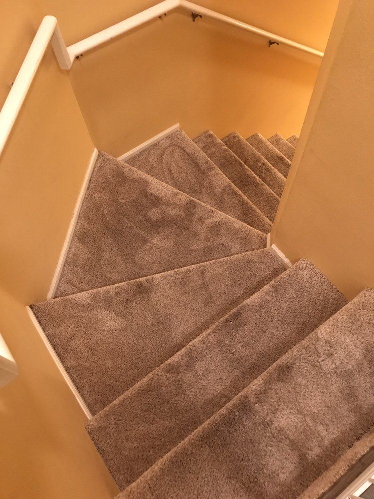 Carpeted stairwell with beige walls and white handrails, viewed from the top down.