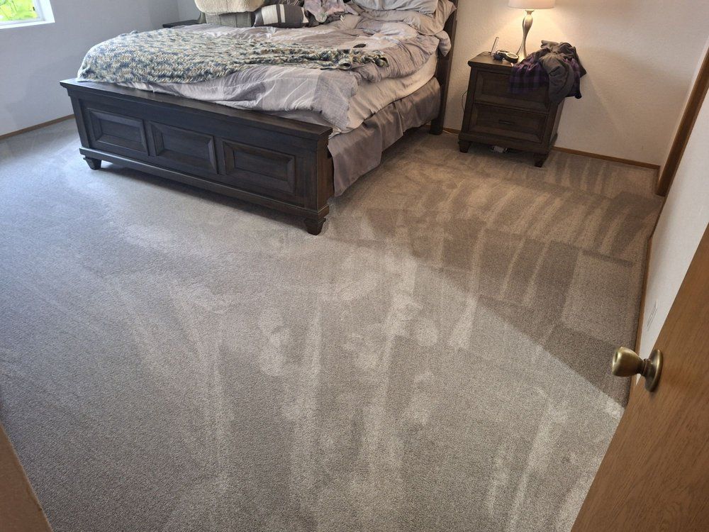 Bedroom with a dark wood bed and bedside table on light carpet, showing visible vacuum or carpet-cleaning marks.