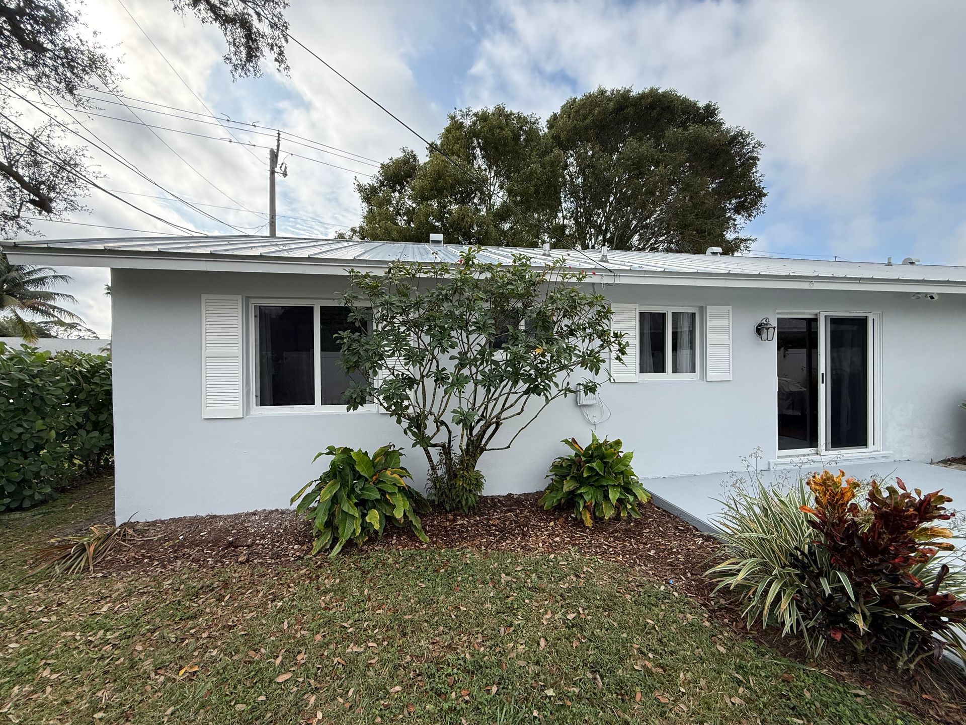 Single-story white house with a tree and shrubs in front, under a cloudy sky